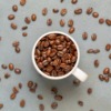 コーヒーカップの中にコーヒー豆が溢れ、散りばめられている画像